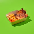 Grilled pork steak with garnish in paper box. Barbecue meat with French fries. Fast food in minimal style on green background. Royalty Free Stock Photo