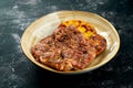 Grilled pork steak with spices and potato garnish, served in a plate on a dark background. Appetizing meat dish, Close up, Royalty Free Stock Photo