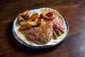 Grilled pork steak with spices and potato garnish, served in a plate with pickled onions, cucumber and red sauce on a wooden Royalty Free Stock Photo