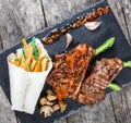 Grilled pork steaks with herbs, asparagus, garlic, mushrooms and potato fry on stone slate background on wooden background Royalty Free Stock Photo