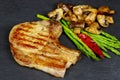 Grilled pork steaks with herbs, asparagus, mushrooms on stone slate background Royalty Free Stock Photo