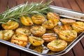 grilled potatoes garnished with rosemary on a mirrored serving tray