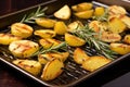 grilled potatoes on metal tray, scattering of rosemary sprigs