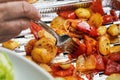 Grilled potatoes and tomatoes served on aluminium foil tray straight from grill, closeup detail on silver fork in vegetables