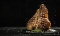 Grilled Premium Dry Aged T-bone Steak or porterhouse steak adding salt in a freeze motion on black background. USDA Prime Beef.