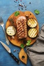 Grilled ribeye beef steak with vegetables, herbs and spices on the cutting Board. Blue rustic background, top view, flat lay. Royalty Free Stock Photo