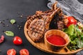 Grilled Ribeye Steak on bone and vegetables with fresh salad and bbq sauce on cutting board over black stone background. Hot Meat