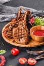 Grilled Ribeye Steak on bone and vegetables with fresh salad and bbq sauce on cutting board over black stone background Royalty Free Stock Photo