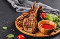 Grilled Ribeye Steak on bone and vegetables with fresh salad and bbq sauce on cutting board over black stone background Royalty Free Stock Photo