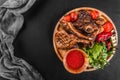 Grilled Ribeye Steak on bone and vegetables with fresh salad and bbq sauce on cutting board over black stone background Royalty Free Stock Photo