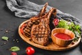 Grilled Ribeye Steak on bone and vegetables with fresh salad and bbq sauce on cutting board over black stone background. Royalty Free Stock Photo