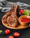 Grilled Ribeye Steak on bone and vegetables with fresh salad and bbq sauce on cutting board over black stone background. Royalty Free Stock Photo