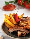 Grilled ribs with French fries and vegetables on the grey background. Shallow depth of field. Vertical orientation Royalty Free Stock Photo