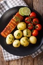 grilled salmon and boiled new potatoes with butter, tomatoes close-up on a plate. vertical top view Royalty Free Stock Photo