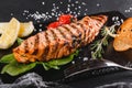 Grilled salmon fillet garnished with spinach, lemon, herbs on on stone board on black table surface. Hot fish dish Royalty Free Stock Photo