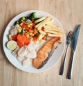 Grilled salmon fish and baked cod fish decorated with various vegetables corn carrot peas lemon french fries and sauces Royalty Free Stock Photo