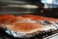 Grilled salmon on the flaming grill. Fresh raw salmon fillet on wooden board wrapped in foil cooking on grill.