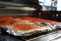 Grilled salmon on the flaming grill. Fresh raw salmon fillet on wooden board wrapped in foil cooking on grill.