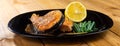 Grilled salmon steak with lemon slice and herbs in a black plate on a wooden background Royalty Free Stock Photo