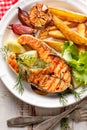 Grilled salmon steak, a portion of grilled salmon with fresh lettuce and potato wedges on a white ceramic plate on a wooden rustic Royalty Free Stock Photo