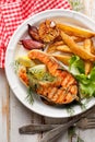 Grilled salmon steak, a portion of grilled salmon with fresh lettuce and potato wedges on a white ceramic plate Royalty Free Stock Photo