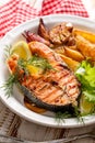 Grilled salmon steak, a portion of grilled salmon with fresh lettuce and potato wedges on a white ceramic plate on a wooden rustic Royalty Free Stock Photo