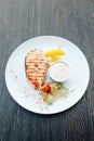 Grilled salmon steak with sauce and lemon on a white plate. Background wooden table Royalty Free Stock Photo
