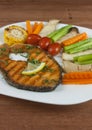 Grilled salmon steak slides until cooked, placed on a white plate with lemon on fish and vegetables, placed around the dish on a