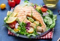 Grilled salmon steak with vegetables, tomatoes, arugula and lettuce side dish salad on plate, blue table background, top view Royalty Free Stock Photo