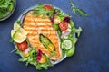 Grilled salmon steak with vegetables, tomatoes, arugula and lettuce side dish salad on plate, blue table background, top view Royalty Free Stock Photo