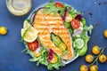 Grilled salmon steak with vegetables, tomatoes, arugula and lettuce side dish salad on plate, blue table background, top view Royalty Free Stock Photo