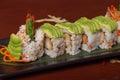 Grilled salmon sushi wrapped with avocado, prawn tempura and cheese on wooden table. Isolated image