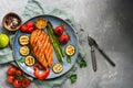 Grilled salmon with vegetables zucchini, asparagus, tomato, sweet pepper on a plate, gray background. Top view, flat lay,copy