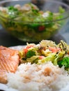 Grilled salmon, white rice and vegetables on white plate at restaurant terrace