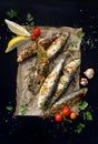 Grilled sardines on paper and a black background, top view.