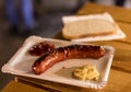 A grilled sausage on a paper plate with mustard and ketchup and a slice of bread, a typical meal sold at outdoor Christmas markets