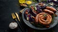 Grilled sausages, and baked red cabbage with cheese, rosemary and cranberries on a black plate. Traditional German dish. Royalty Free Stock Photo