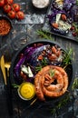 Grilled sausages, and baked red cabbage with cheese, rosemary and cranberries on a black plate. Traditional German dish. Royalty Free Stock Photo