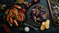 Grilled sausages, and baked red cabbage with cheese, rosemary and cranberries on a black plate. Traditional German dish. Royalty Free Stock Photo