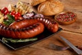 Grilled sausages with vegetables, spices and bread in black plate on wooden table. Close up macro view