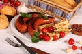 Grilled sausages with vegetables, spices and bread in white plate on white wooden table