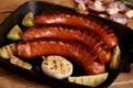 Grilled sausages with vegetables and spices in a pan on wooden background