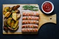 Grilled sausages on a wooden chopping Board. Fried potatoes, rosemary, tomato ketchup. Unhealthy diet. Dark background Royalty Free Stock Photo