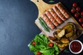 Grilled sausages on a wooden chopping Board. Fried potatoes, rosemary, tomatoes, green lettuce leaves, tomato ketchup. Unhealthy Royalty Free Stock Photo