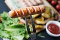 Grilled sausages on a wooden chopping Board. Fried potatoes, rosemary, tomatoes, green lettuce leaves, tomato ketchup. Unhealthy Royalty Free Stock Photo