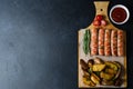 Grilled sausages on a wooden chopping Board. Fried potatoes, rosemary, tomatoes, tomato ketchup. Unhealthy diet. Dark background. Royalty Free Stock Photo