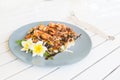 Grilled shrimps or prawns with fried vegetables on the light blue plate. Decorated with frangipani flower. Fork and knife on the Royalty Free Stock Photo