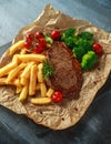 Grilled sirloin steak with potato fries, broccoli and cherry tomatoes on crumpled paper Royalty Free Stock Photo