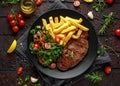 Grilled sirloin steak with potato fries and vegetables, tomato salad in a black plate. rustic table Royalty Free Stock Photo