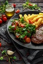 Grilled sirloin steak with potato fries and vegetables, tomato salad in a black plate. rustic table Royalty Free Stock Photo